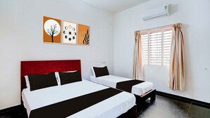 A hotel room with two beds, a red headboard, a window with curtains, and wall art. - Townhouse Mysuru Sand Museum (Mysore)
