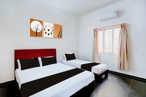 Hotellihuone, jossa on kaksi sänkyä, punainen pääty, ikkuna verhoilla ja seinätaidetta.