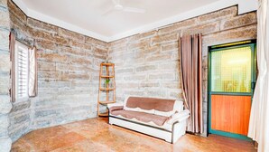 A room with a stone wall, a white sofa, a wooden ladder, and a window with curtains. - Townhouse Mysuru Sand Museum (Mysore)