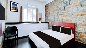 A hotel room with a brick-patterned wall, a bed with a red headboard, a window with blinds, a chair, and a framed picture on the wall. - Townhouse Mysuru Sand Museum (Mysore)