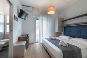 Una camera d'albergo con un letto, una televisione a parete, una scrivania con una sedia e una finestra con tende.