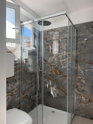 Un bagno moderno con doccia vetrata, pareti in marmo e un water bianco.