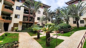 A courtyard with a paved walkway, palm trees, and a multi-story building with balconies. - Life Resort - Beira do Lago em Brasilia (Brasília)