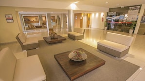 A hotel lobby with seating areas, a reception desk, and a glass wall with a view. - Life Resort - Beira do Lago em Brasilia (Brasília)