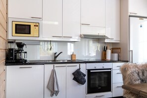 A modern kitchen with white cabinets, a microwave, a coffee machine, and an oven. - Kaakkoishovi by Aavalevi (Levi)