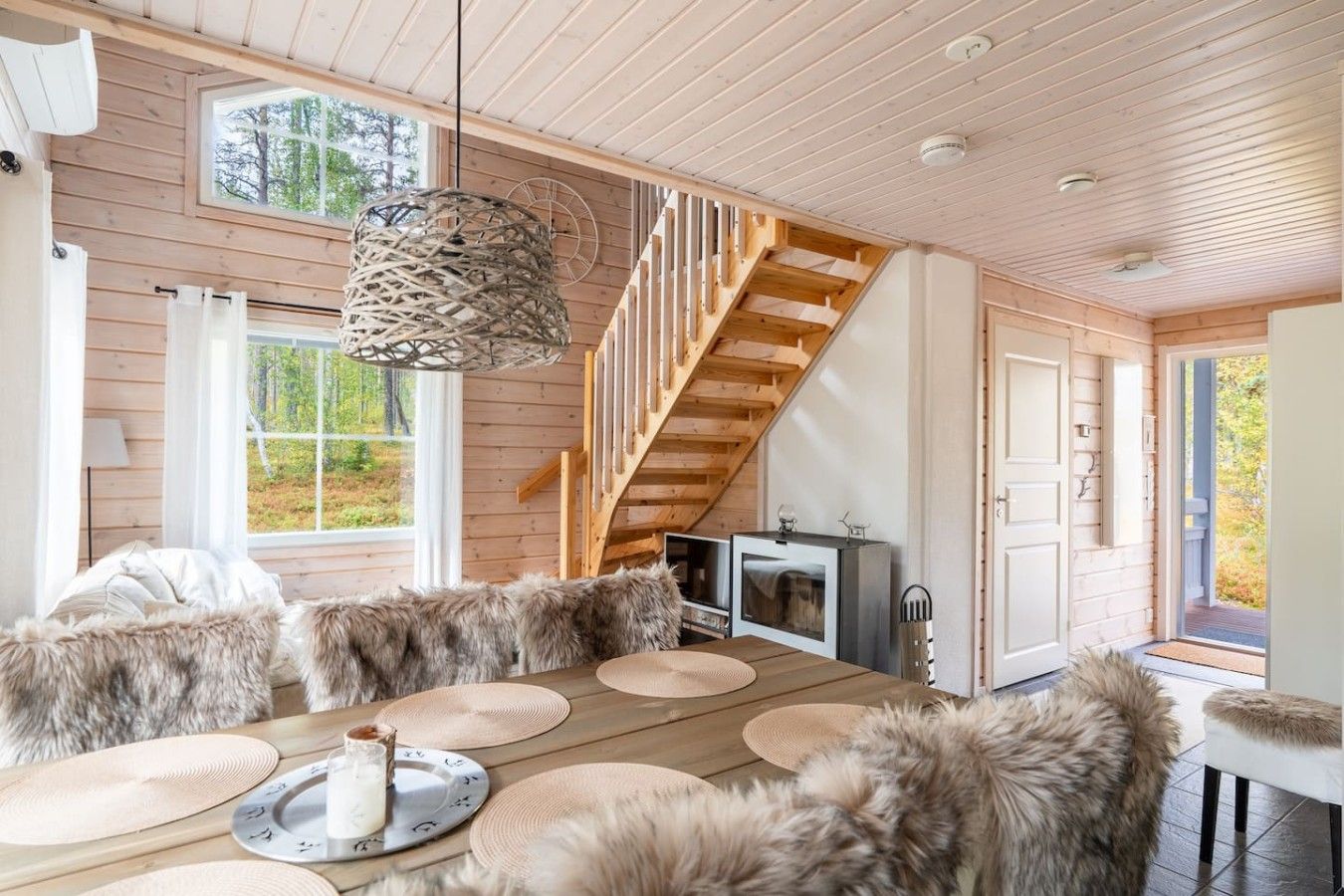 Een houten interieur met een eethoek, een trap en uitzicht op het omliggende landschap.