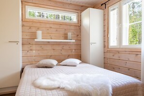 Ein Schlafzimmer mit einem Bett, Kissen, einer flauschigen weißen Decke, einer Holzzahlung und einem Fenster.
