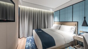 A hotel room with a bed, a desk with a telephone, a TV, and a window with curtains. - Echarm Hotel (Guilin)
