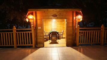 Una estructura de madera con una mesa y sillas, piso de baldosas y una cerca de madera.