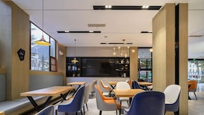 Interior moderno de café com mesas e cadeiras de madeira, iluminação pendente e vista pela janela.