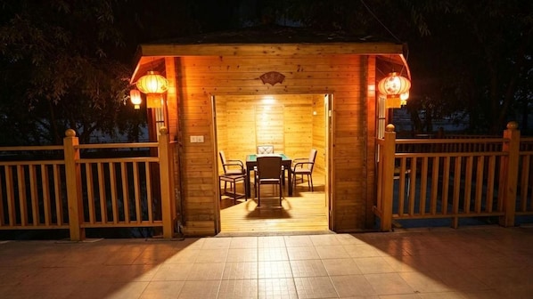 Een houten constructie met een tafel, stoelen, een betegelde vloer en een houten omheining.