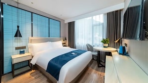 Quarto de hotel moderno com cama grande, mesas de cabeceira, escrivaninha e uma cadeira.