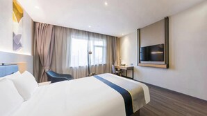Quarto de hotel com cama, escrivaninha, cadeira, televisão e janela com cortinas.