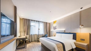Quarto de hotel com cama, mesa de cabeceira, televisão e escrivaninha com cadeira.