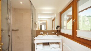 Een moderne badkamer met een douchecabine van glas, een wastafel met spiegel en een raam met uitzicht op de omgeving.