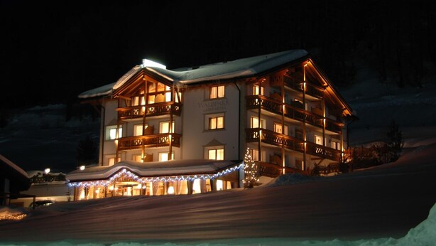 Een hotel met meerdere verdiepingen, balkons, besneeuwde omgeving en decoratieve verlichting.
