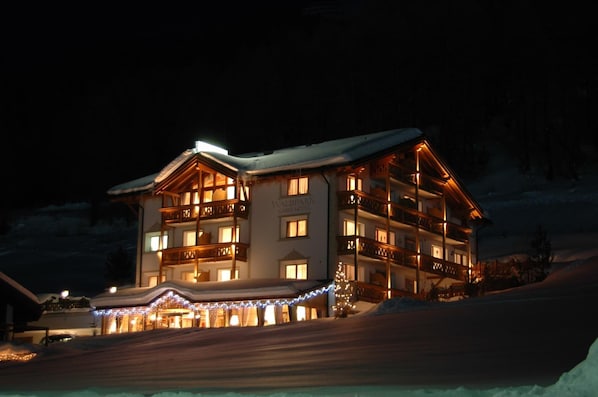 Hotel de vários andares com varandas, paisagem coberta de neve e luzes decorativas.