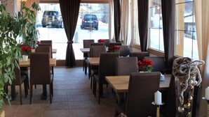 Een restaurant met houten balken in het plafond, grote ramen met gordijnen, en tafels met stoelen.