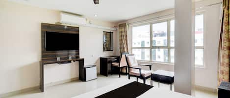 Quarto de hotel com televisão de tela plana, escrivaninha, cadeira, ventilador de teto e uma grande janela.