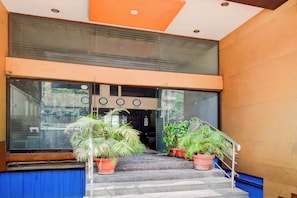 Entrada de un hotel con una doble escalera, plantas en macetas y un puerta de cristal con relojes que marcan diferentes husos horarios.