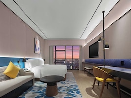 Una habitación de hotel moderna con cama, sofá, escritorio y vistas a la ciudad al atardecer.