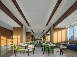 Un comedor interior amplio con varias mesas y sillas, un suelo estampado y grandes ventanales que ofrecen vistas del paisaje urbano.