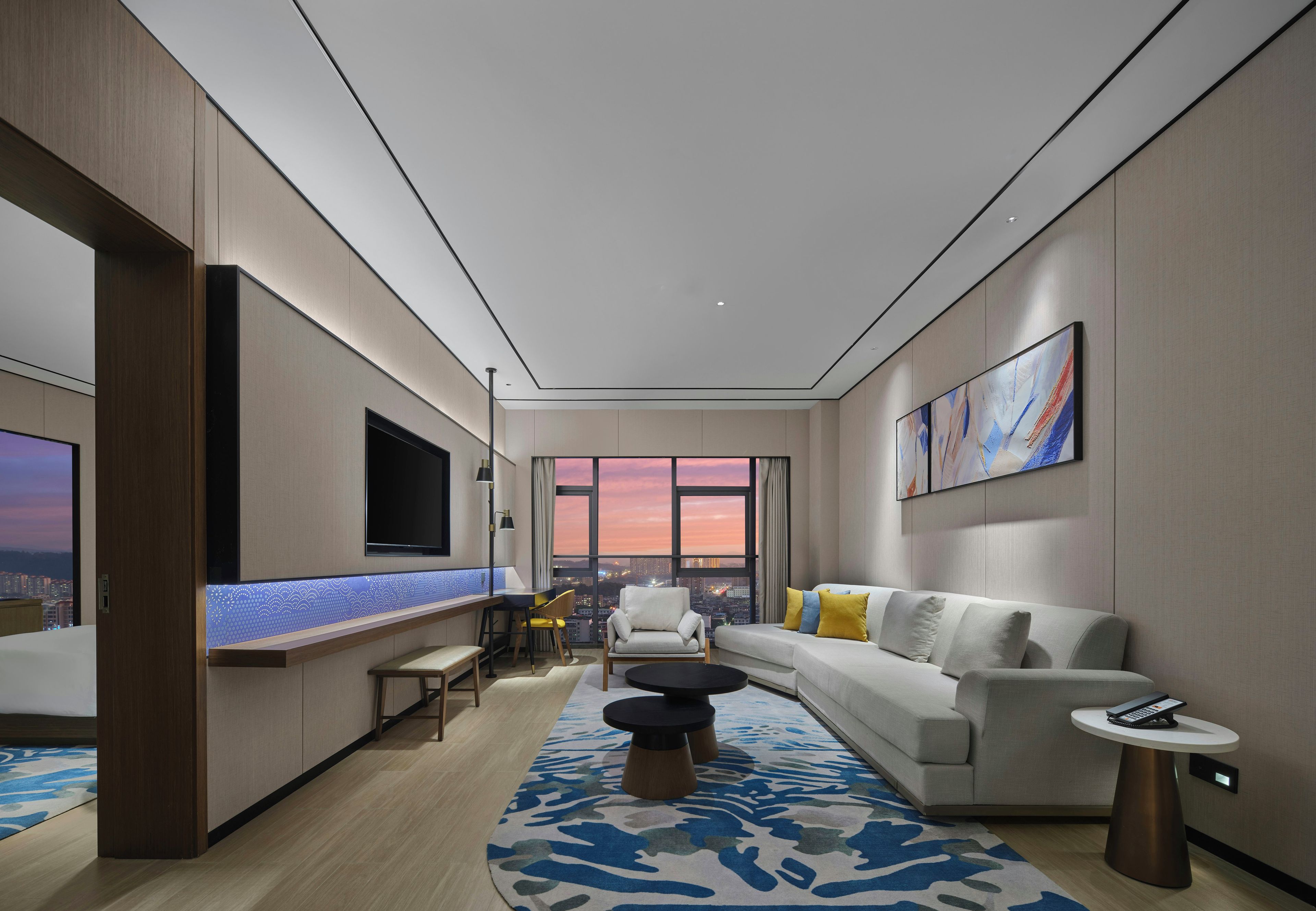 A modern living room with a large window, a sofa, a coffee table, and a TV mounted on the wall.
