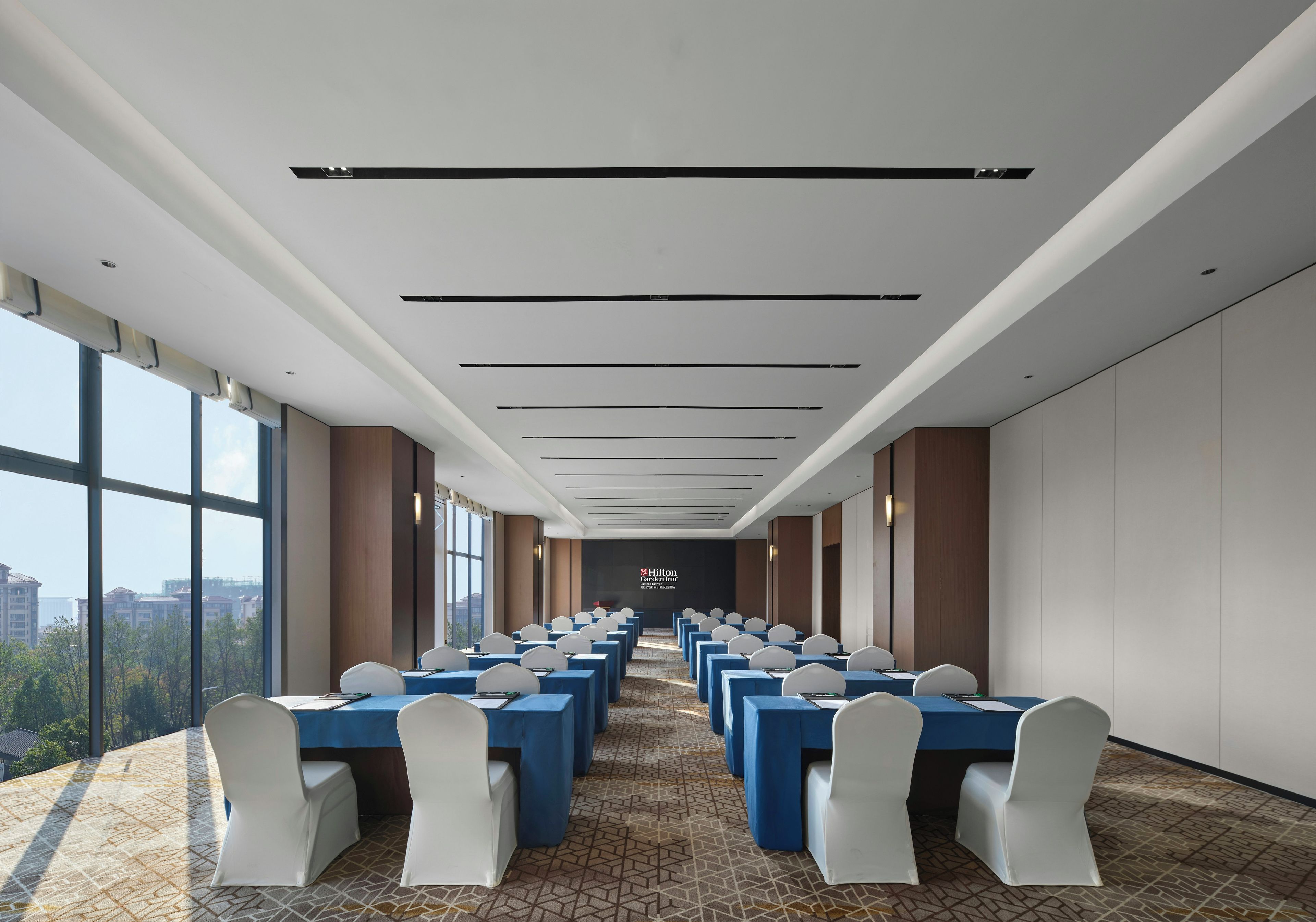 A conference room with rows of tables and chairs, large windows, and a view of the cityscape.