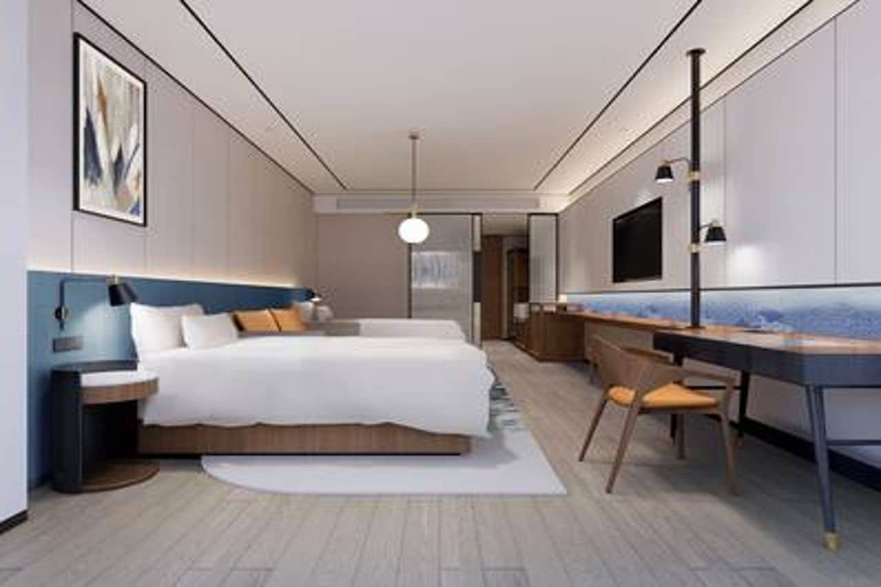 A modern bedroom with a bed, bedside table, desk, chair, and a large mirror.
