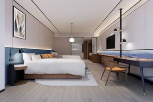Un dormitorio moderno con cama, mesita de noche, escritorio, silla y un espejo grande.