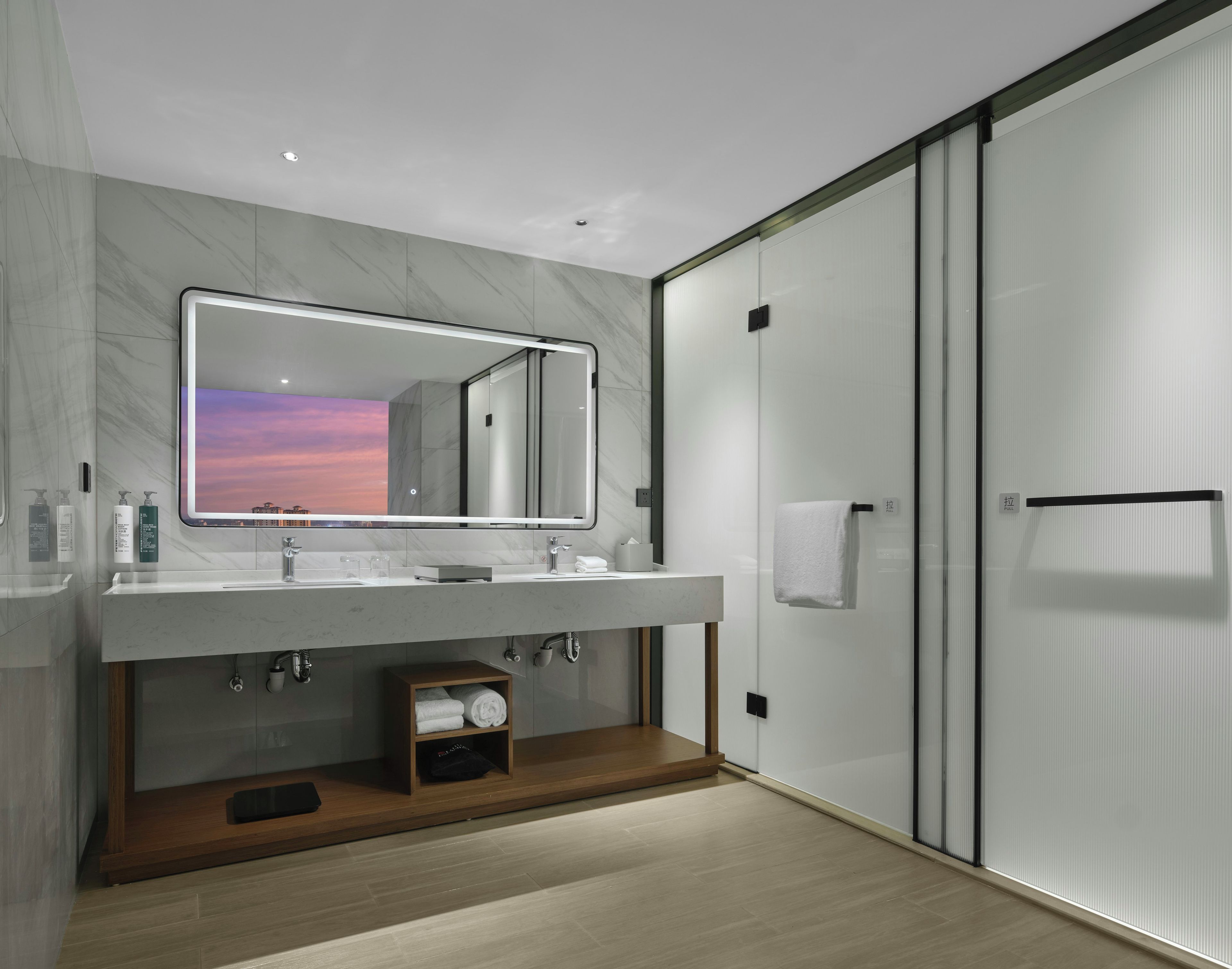 A modern bathroom with a large mirror, two sinks, a towel rack, and a wooden shelf.