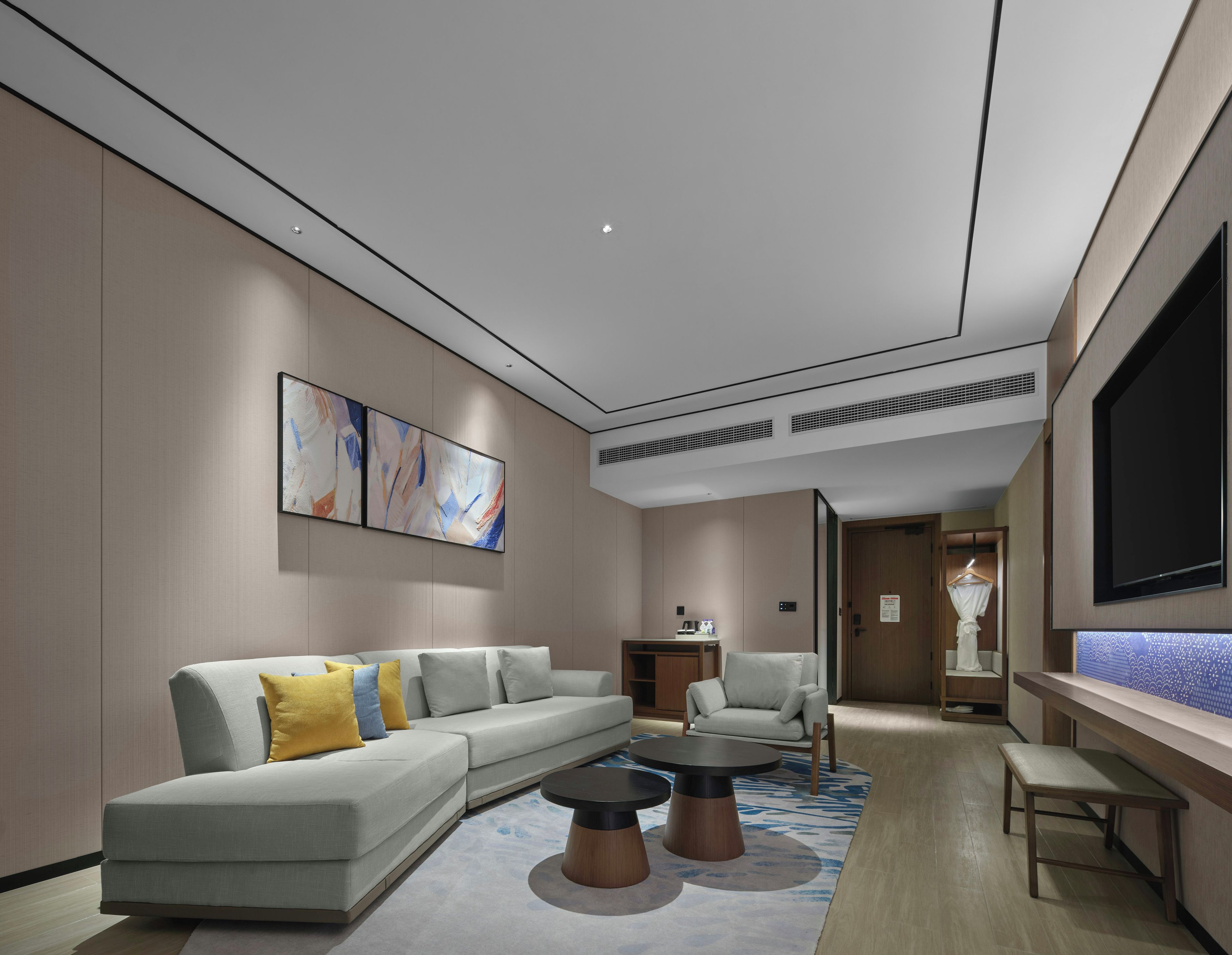 A modern living room with a sectional sofa, two round coffee tables, a flat-screen TV, and abstract wall art.