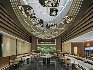 Um lobby moderno com área de estar, uma tela grande exibindo uma paisagem e um design de teto singular.