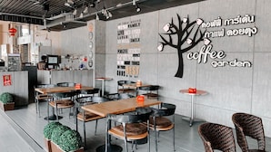 Café tipo jardín con mesas y sillas, una pared con citas motivacionales y un letrero en idioma extranjero.