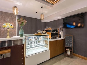Interior moderno de una cafetería con un expositor de vidrio, máquinas de café y un menú en una pizarra.