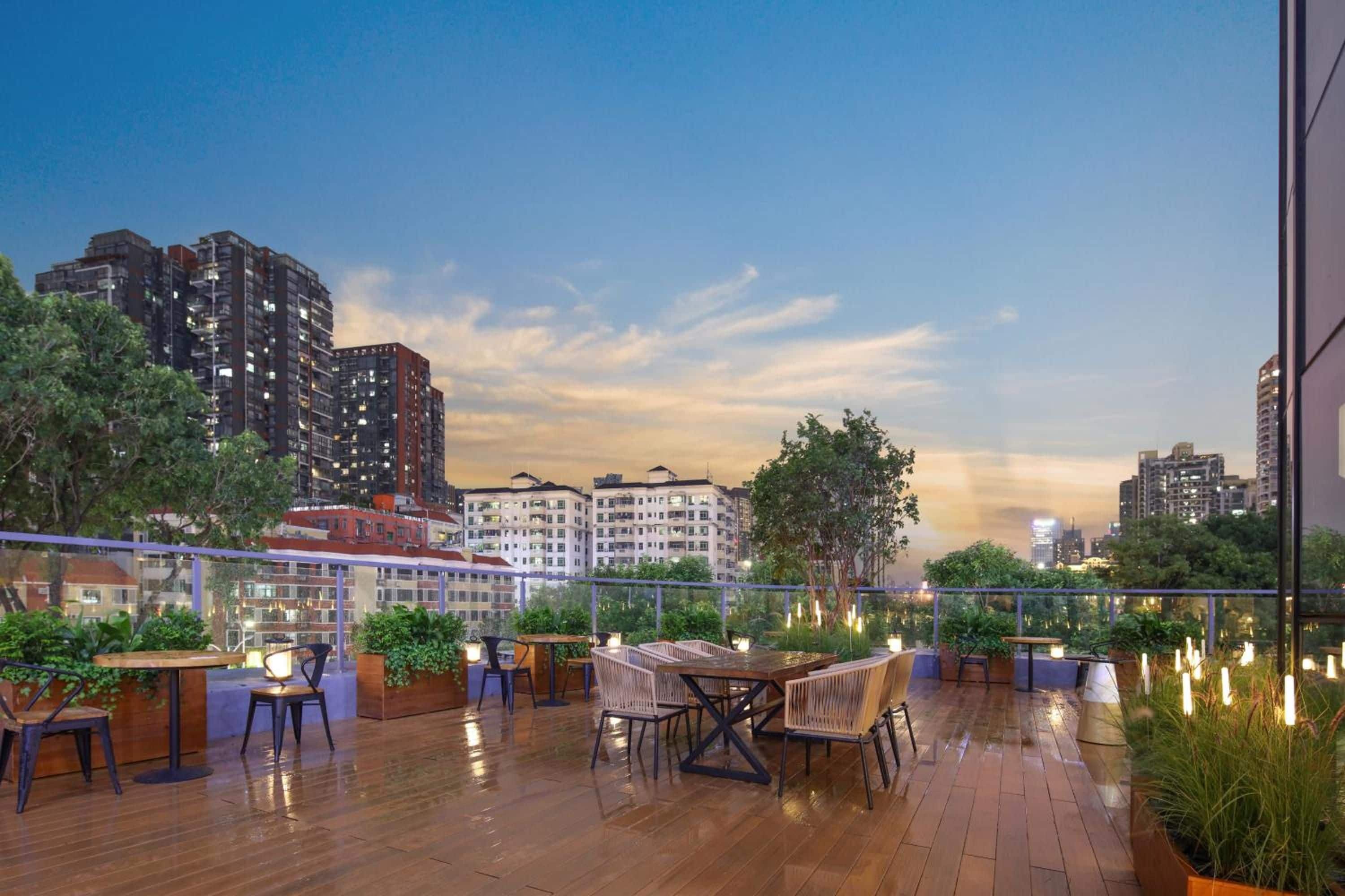 An outdoor terrace with wooden flooring, tables, chairs, and potted plants.
