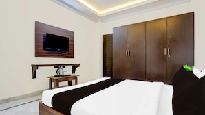 Une chambre d’hôtel avec un lit, un téléviseur fixé au mur, une armoire en bois et une petite table avec une bouilloire.