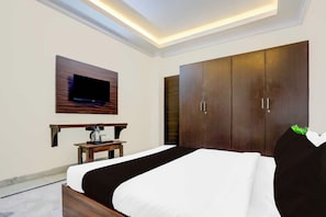 Une chambre d’hôtel avec un lit, un téléviseur fixé au mur, une armoire en bois et une petite table avec une bouilloire.