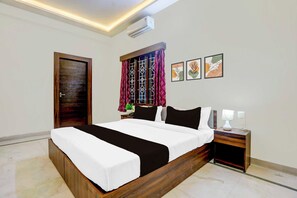 A bedroom with a bed, bedside tables, a nightstand, a window with curtains, and wall art. - Townhouse Oak Bangalore Central Silk (Bengaluru)