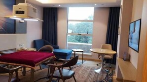 Et hotelværelse med seng, skrivebord, stol, lille bord og et vindue med udsigt.