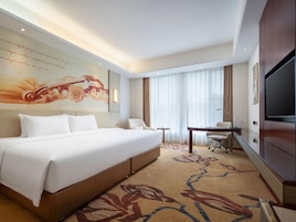 Una habitación de hotel con una cama grande, un escritorio, una silla, un televisor y un mural decorativo en la pared.