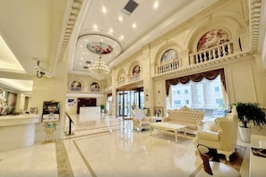Um hall amplo com um lustre imponente, um balcão de recepção e uma área de estar com sofás confortáveis.