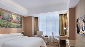 Una habitación de hotel con una cama grande, un escritorio, una silla, una mesita y un televisor.