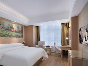 Quarto de hotel com uma cama grande, uma escrivaninha, uma cadeira, uma mesinha de centro e uma televisão.
