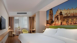 Quarto de hotel com uma cama grande, uma escrivaninha, uma cadeira e um quadro de um edifício histórico.