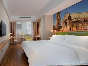 Een hotelkamer met een groot bed, een bureau, een stoel en een schilderij van een historisch gebouw.