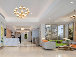 Een ruime lobby met een receptiebalie, een grote kroonluchter en een zithoek met een bank en fauteuils.