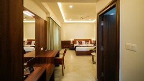 Habitación de hotel con escritorio de madera, cama con cabecera, espejo y ventilador de techo.