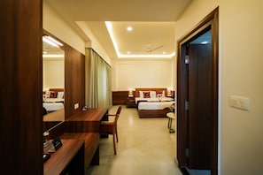 A hotel room with a wooden desk, a bed with a headboard, a mirror, and a ceiling fan. - Zip By Spree Hotels Purple Orchid (Bengaluru)