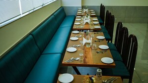 Un comedor con una mesa larga dispuesta para varios comensales, un banco acolchado verde y sillas colocadas alrededor de la mesa.